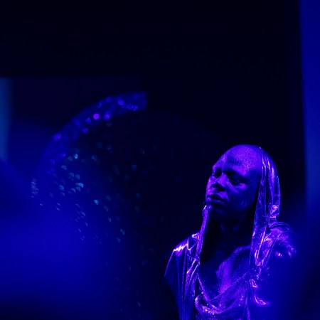 Eine Person of Colour, Augen geschlossen, Kapuze, violett-blaue Lichtstimmung